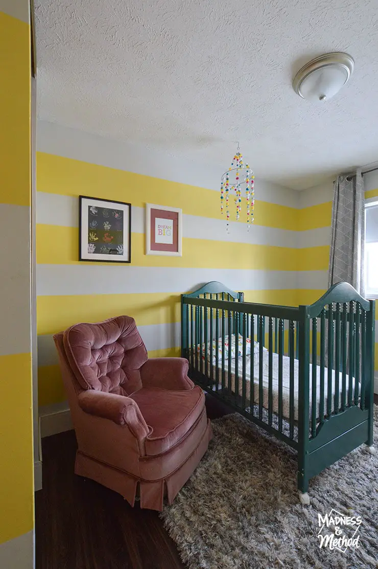 yellow white striped wall nursery with pink chair and green crib