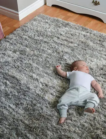 baby on shag gray rug with pink chair nearby