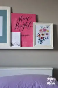 Bright coloured prints on a photo ledge behind a bed
