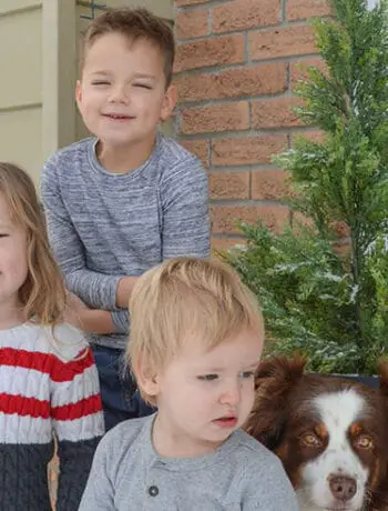 three kids and dog standing near evergreen tree