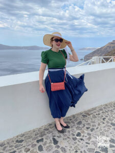 green shirt navy skirt and coral purse with sun hat in santorini