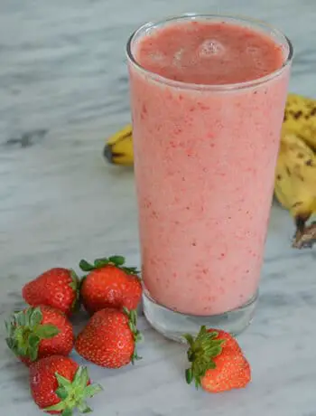 pink smoothie in glass with marble counters strawberries and bananas