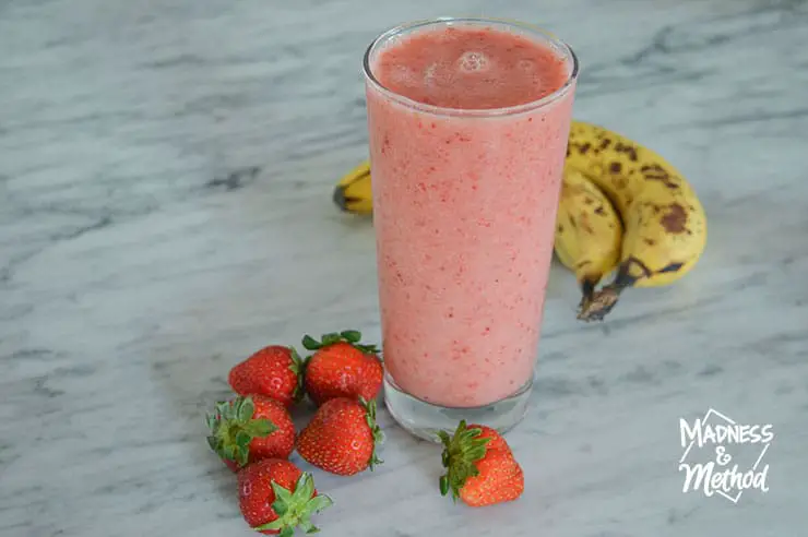 pink smoothie in glass with marble counters strawberries and bananas