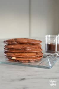 stack of triple chocolate pancakes next to syrup jar