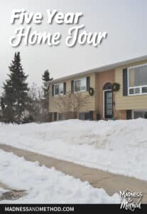 beige raised ranch house in snow with sidewalk